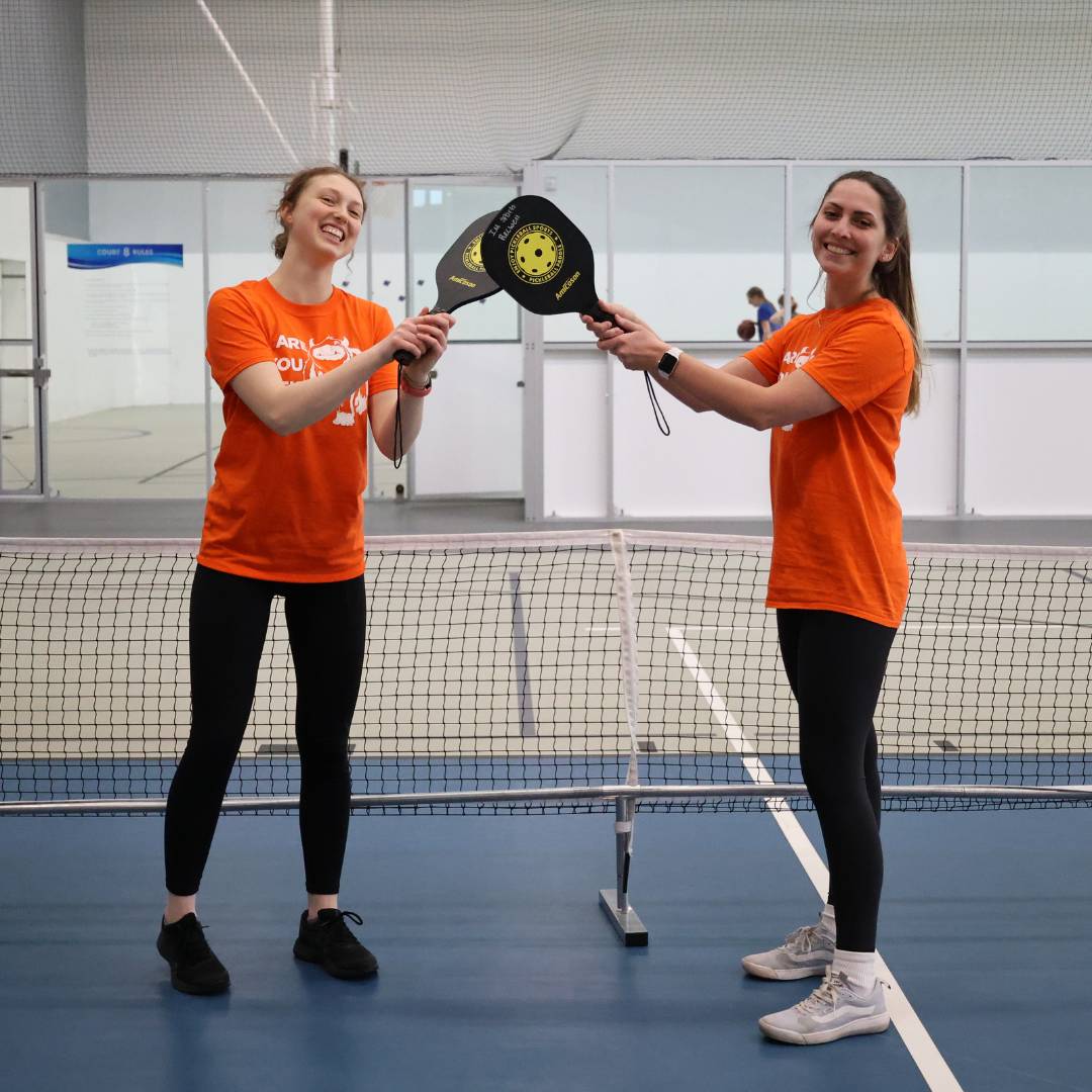 Two WIT peer educators with pickle ball rackets and matching shirts